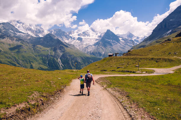 Grandfather and grandson with backpack hiking on mountain trail high in Pennine Alps near Zinal in the summer, back view. Val d' Anniviers, Valais, Switzerland