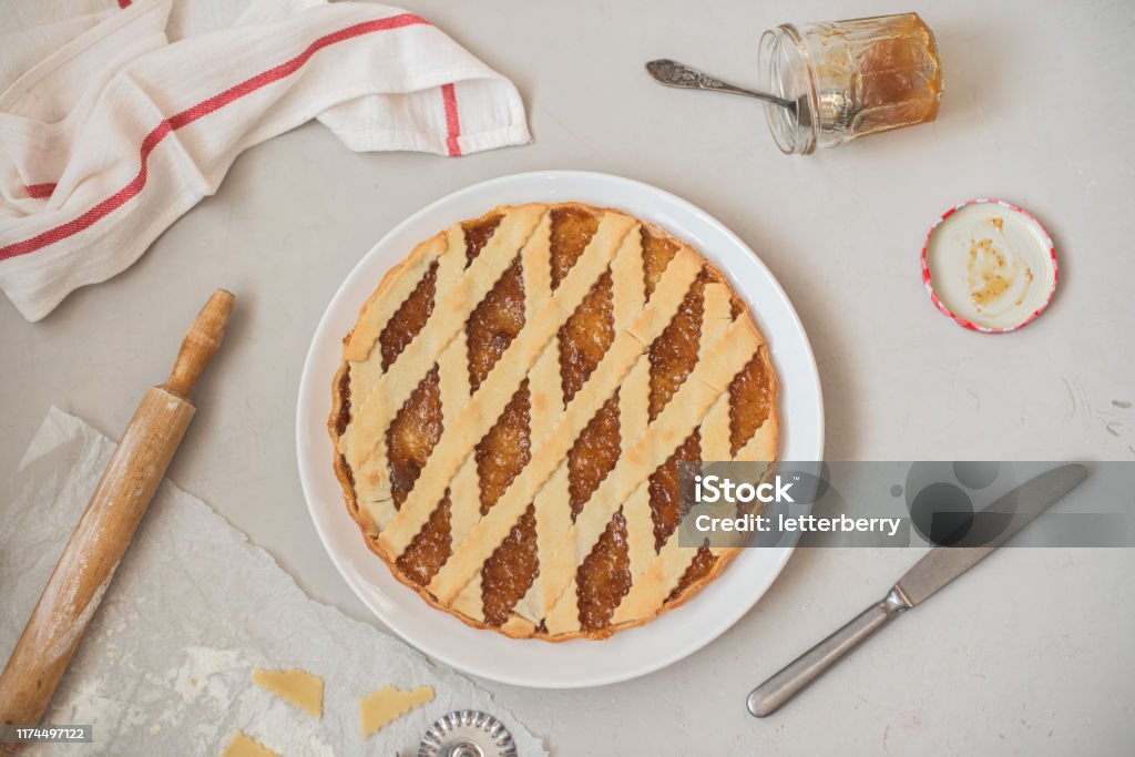 Cooking Italian figs jam tart Crostata on a white plate Cooking Italian figs jam tart Crostata on a white plate, rolling pin, a jar of jam, a knife and a napkin on a light gray background Crostata Stock Photo