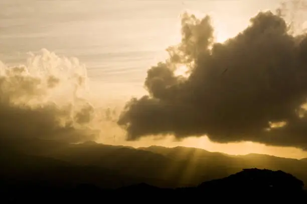 Light rays burst through the clouds and spill onto the silhouetted mountain range below