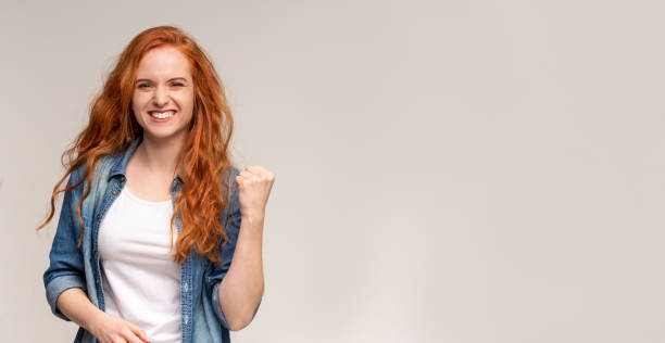 Emotional girl smiling and raising clenched fist in the air Emotional ginger girl smiling and raising clenched fist in the air, feeling excited, Panorama with copy space raised fist photos stock pictures, royalty-free photos & images