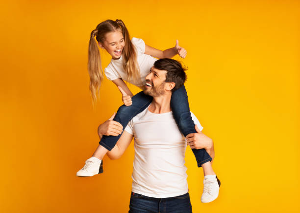 padre che dà a sua figlia piggyback ride gestiuring thumbs-up in studio - clothing love family with one child parent foto e immagini stock