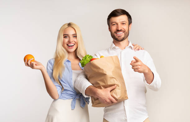 istock Couple Holding Grocery Bag Pointing Finger At Camera On White Background 1174502374