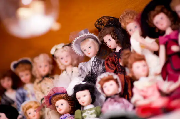 A collection of antique dolls in retro dresses. One doll is in focus, the rest are in defocus. Concept, background