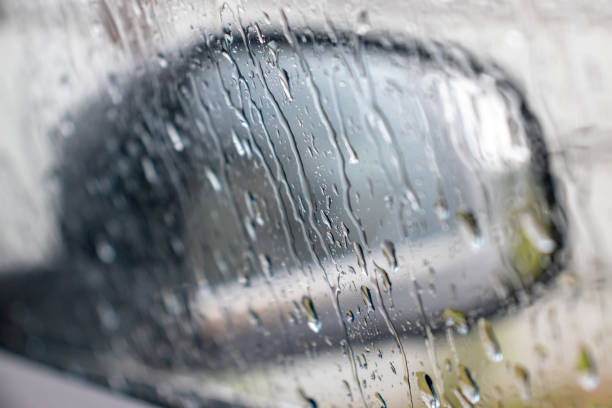 gouttes de pluie roulant sur la fenêtre dans la tempête, et un miroir noir brouillé de vue de côté de voiture sur un fond, fermez vers le haut - mirror reflection blues glass photos et images de collection