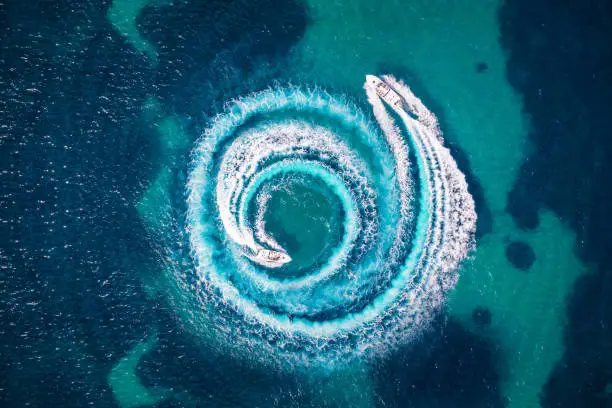 Aerial view of two motorboats forming a circle of waves and bubbles with their engines over turquoise sea