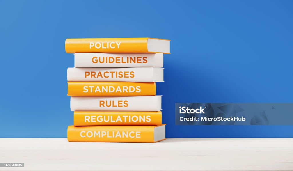 Books of Compliance And Regulations In Front Grey Wall Books of compliance, regulations, rules and guidelines are sitting on top of each other. The books have unique texts on their spines related to compliance subject. Strategy Stock Photo