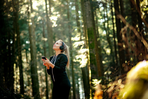 Young Woman Listening To Music With Headphones and Mobile Phone in Nature and Looking Up.