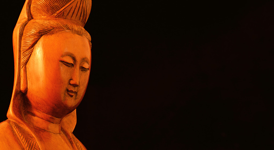 Buddhist religion and meditation. Kannon of Guanyin, the Goddess of Mercy, wooden statuette on black background
