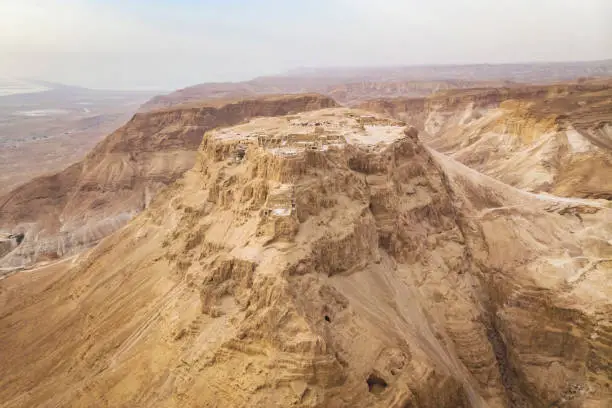 Scenic view of the cliff with a flat platform on the top shot from the air. Ancient isolated settlement on the plateau in Judean desert, Israel. Archaeological works. Ruins of ancient fortification.
