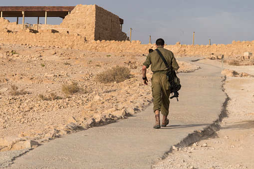 Back view of military going alone among deserted territory somewhere in middle east. Masada fortification, Israel, war trainning. Israel, October 23, 2018