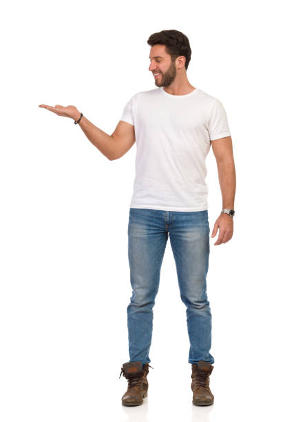 istock Smiling Man In Jeans And White T-shirt Is Standing With Hand Raised And Presenting. Front View. 1174534634