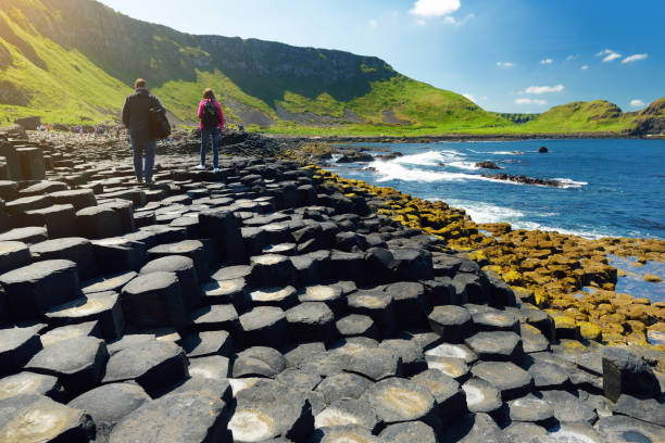 dos turistas caminando en giants causeway, un área de piedras de basalto hexagonal, condado de antrim, irlanda del norte. famosa atracción turística, patrimonio de la humanidad de la unesco. - northern ireland fotos fotografías e imágenes de stock