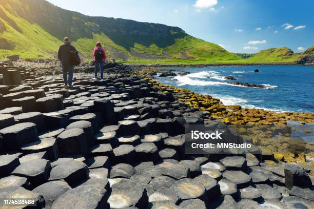 Two Tourists Walking At Giants Causeway An Area Of Hexagonal Basalt Stones County Antrim Northern Ireland Famous Tourist Attraction Unesco World Heritage Site Stock Photo - Download Image Now