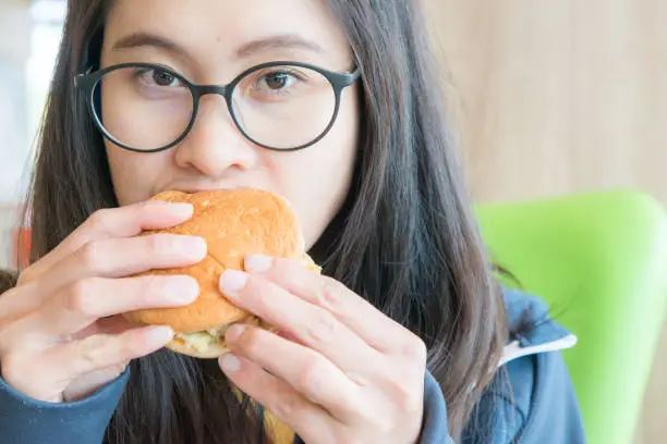 Photo of Young Asian woman bite a piece of small crispy chicken burger in her hand.