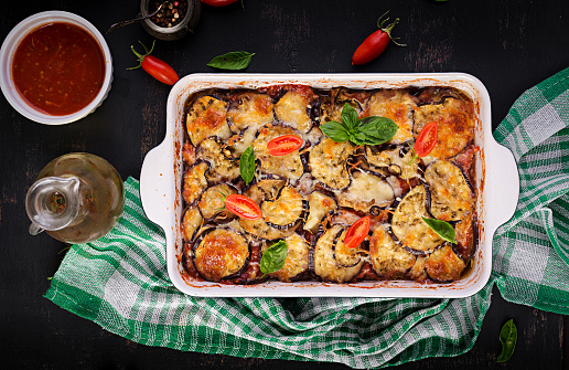 Baked eggplant with cheese on a dark wooden table. Parmigiana melanzane. Top view. Italian cuisine. Copy space