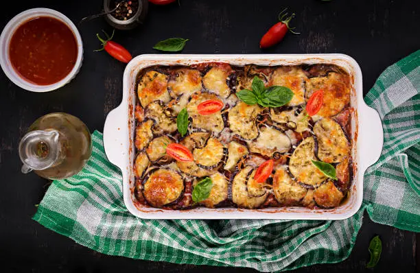 Photo of Baked eggplant with cheese on a dark wooden table. Parmigiana melanzane. Top view. Italian cuisine. Copy space