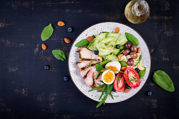istock Ketogenic diet. Keto brunch. Boiled egg, pork steak and olives, cucumber, spinach, brie cheese, nuts and tomato. Top view 1174567772