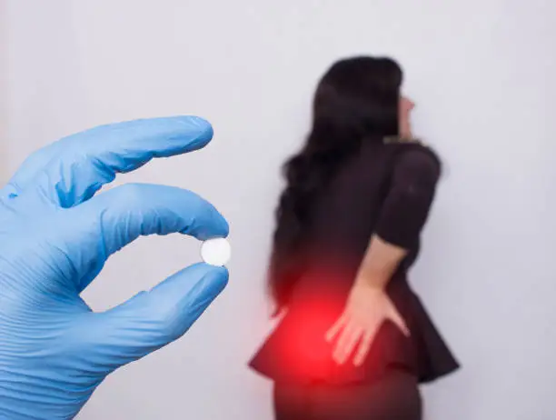 Photo of The doctor holds a pill for back pain, in the background a girl who has a back hernia and osteochondrosis, medicament