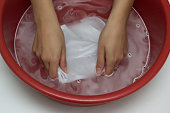 The girl erases a children's white T-shirt in a red basin from stains, cleans from stain remover, close-up, hands, white background