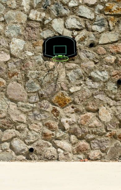 A basketball backboard in black on a stone wall. Solid defence concept. A basketball backboard with green rim on a stone masonry wall with large copy space. impassable limit stock pictures, royalty-free photos & images