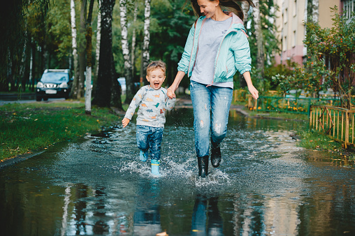 Child with his mother walking on the puddles after the rain. Summer rainy weather concept. The Concept of Family Happiness
