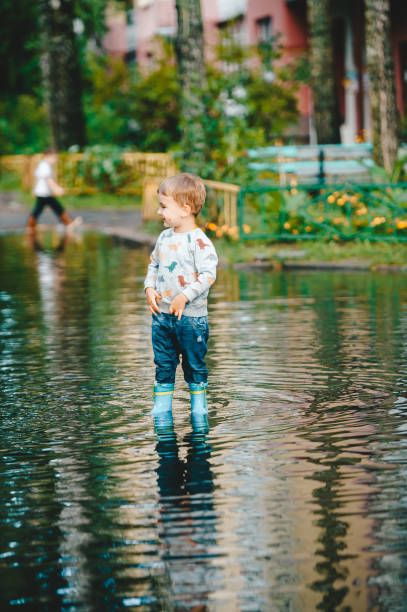 istock Little boy after the rain wearing blue rubber boots stand in puddle. 1174590796
