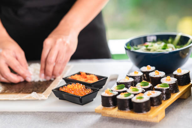 Chef preparing sushi. Chef preparing sushi. Asian woman chef in black uniform, putting rice on nori seaweed, with salmon egg. nori edible seaweed sheet stock pictures, royalty-free photos & images