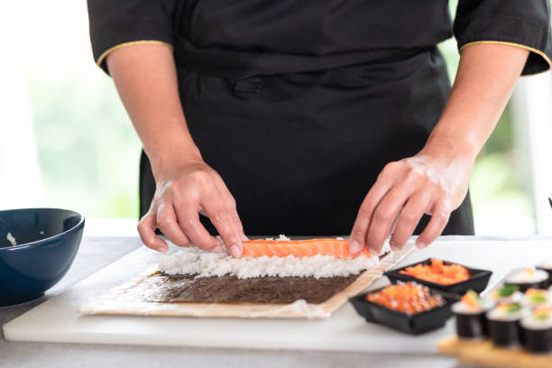 Chef preparing sushi. Chef preparing sushi. Asian woman chef in black uniform, putting raw salmon on rice. nori edible seaweed sheet stock pictures, royalty-free photos & images