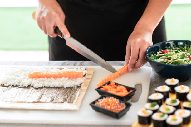Chef preparing sushi. Chef preparing sushi. Asian woman chef in black uniform, cutting another piece of raw salmon to put on nori. nori edible seaweed sheet stock pictures, royalty-free photos & images