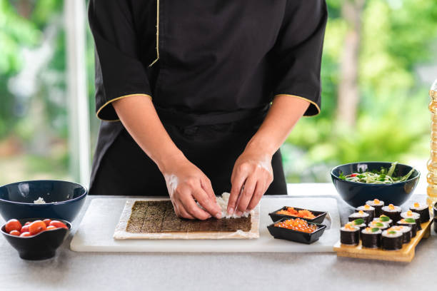 Chef preparing sushi. Chef preparing sushi. Asian woman chef in black uniform, putting rice on nori seaweed. nori edible seaweed sheet stock pictures, royalty-free photos & images