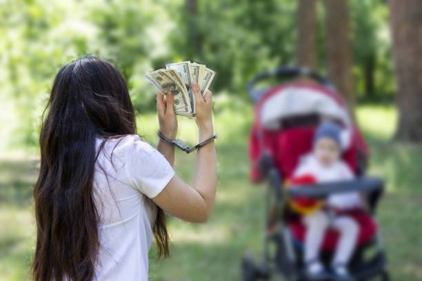 dziewczyna trzyma pieniądze w kajdankach na tle dziecka w wózku, aresztowaniu, areszcie na sprzedaż przez dzieci, handlu dziećmi - underdeveloped zdjęcia i obrazy z banku zdjęć