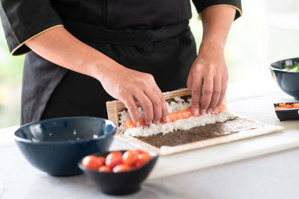 Chef preparing sushi. Chef preparing sushi. Asian woman chef in black uniform, about to roll salmon into sushi. nori edible seaweed sheet stock pictures, royalty-free photos & images
