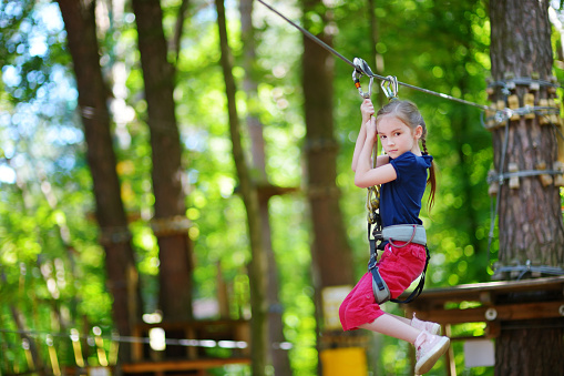Adorable little girl enjoying her time in climbing adventure park on warm and sunny summer day