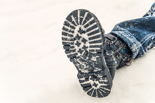 Winter boot on the feet of a boy lying in the snow. Child non-slip shoes.