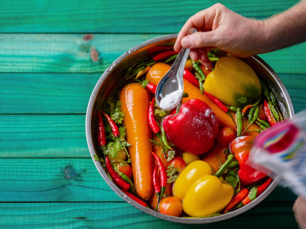 Washing and soaking fresh market vegetables in a water and baking soda solution to safely remove pestiside and other chemical residues. Soaking vegetables in a solution of water with sodium bicarbonate for twenty minutes helps to remove insecticides from the skin of the vegetables, here capsicums, tomatoes, red chili peppers, carrots and coriander are being soaked in the solution before a thorough wash with fresh water afterwards. drenched stock pictures, royalty-free photos & images