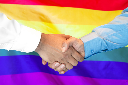 Business handshake on LGBT gay flag background. Men shaking hands and LGBT gay flag on background. Flag of tolerance. Support concept