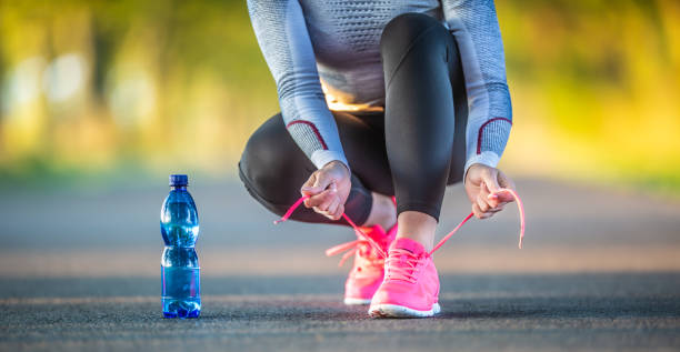 woman runner tying shoelaces before jogging in autumn tree alley park. sports female autumn outfit leggings and thermal underwear. sports drinking regime concept. - shoe tying adult jogging imagens e fotografias de stock