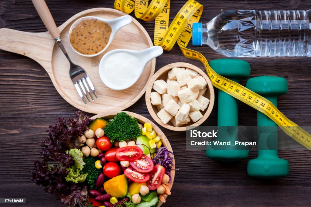 Fresh vegetable salad and healthy food for sport equipment for women diet slimming with measure tap for weight loss on wood background. Healthy Sport Concept Dieting Stock Photo