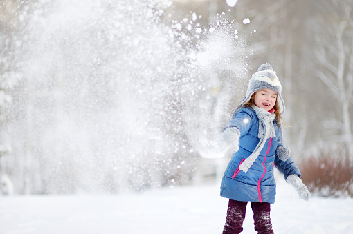 Funny little girl having fun in beautiful winter park during snowfall
