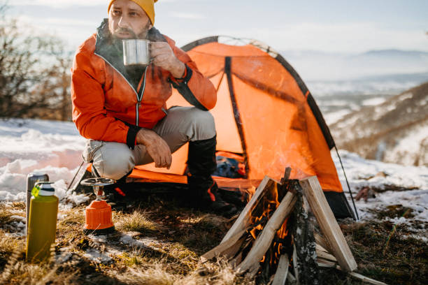 Hot tea the best thing in cold snowy days Mature man drinking hot drink in metal cup near tent on winter camping camping stove photos stock pictures, royalty-free photos & images
