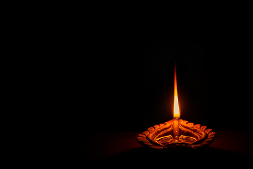 Background picture of traditional diya clay oil lamp lit at dark night on Diwali with copy space in landscape format.