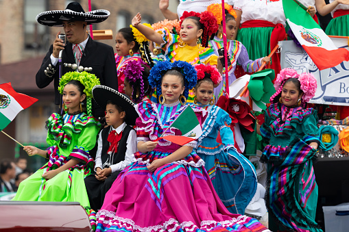 Chicago, Illinois, USA - September 8, 2019: 26th Street Mexican Independence Parade, Mexican girlsand boys, wearing traditional clothing, waving mexican flags on a float, during the parade