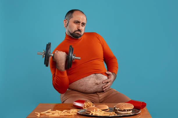 istock Close-up portrait of a middle-aged man with beard, dressed in a red turtleneck, posing with burgers and french fries. Blue background. Fast food 1174646485