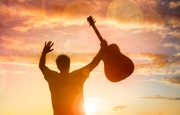 silhouette des gitarristen musiker hält gitarre gegen sonnenuntergang - geistliche musik stock-fotos und bilder