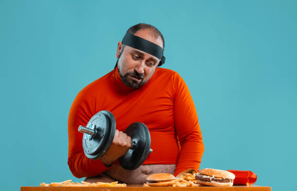 istock Middle-aged man with beard, dressed in a red turtleneck, headband, posing with burgers and french fries. Blue background. Close-up. Fast food 1174647679