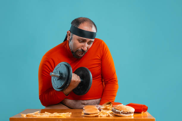istock Middle-aged man with beard, dressed in a red turtleneck, headband, posing with burgers and french fries. Blue background. Close-up. Fast food 1174647727