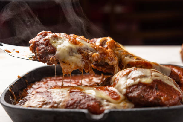 parmegiana steak also known as filet parmegiana in a black iron pan on a wooden white background, cheese and tomato sauce. - healthy eating italian culture traditional culture close up - fotografias e filmes do acervo