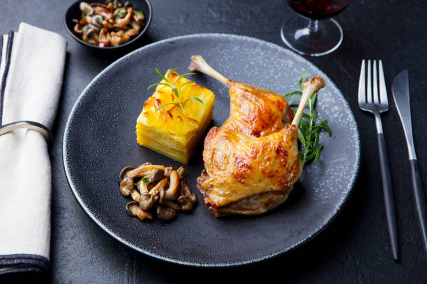 Duck legs confit with potato gratin and mushroom on a plate. Slate background. Duck legs confit with potato gratin and mushroom on a plate. Slate background confit stock pictures, royalty-free photos & images