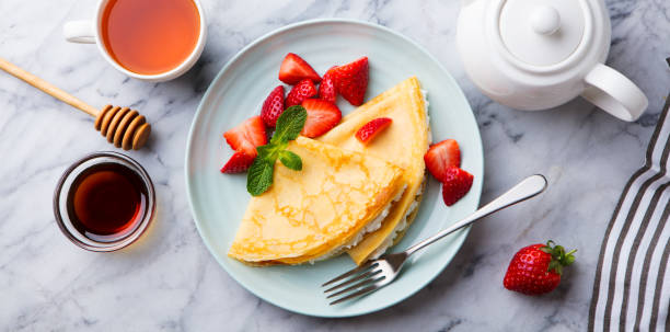 istock Crepes, thin pancakes with cream cheese, ricotta, fresh strawberries. Marble background. Top view. 1174656542