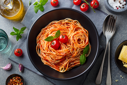 Pasta, spaghetti with tomato sauce in black bowl on grey stone background. Top view